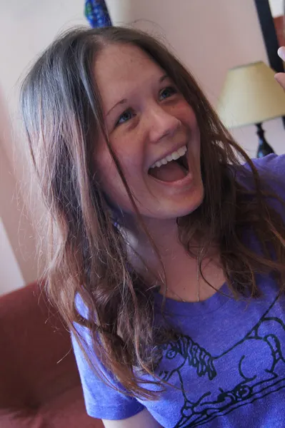 Dagney McKinney portrait of white light brunette with long hair and is laughing with an open mouth and wearing a purple t-shirt with lamp in background