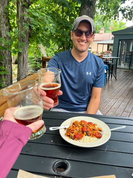 BearWaters Brewing Maggie Valley North Carolina with white brunette male clinking beer glasses with white brunette female over table of food by the creek