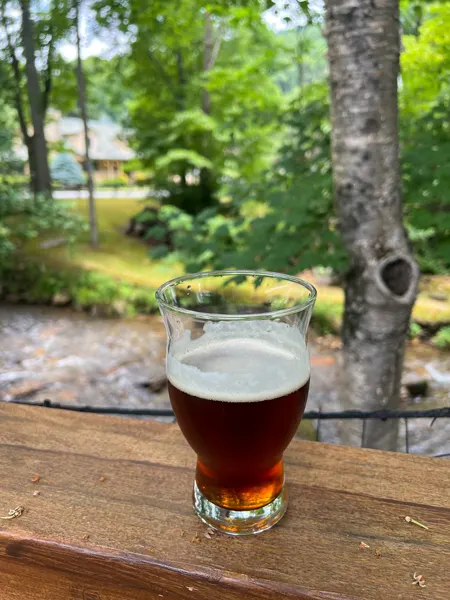 BearWaters Brewing Restaurant Maggie Valley North Carolina with half pour of amber lager on railing overlooking running creek with green trees