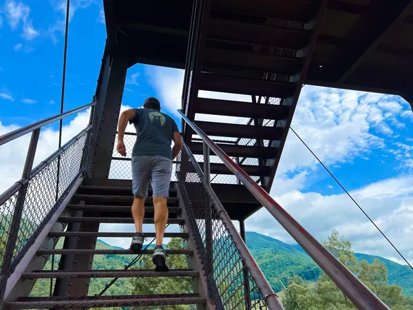 Maggie Valley Soco Crafts Tower with white brunette male in short, tshirt, and hat going up tower steps with mountains in the background