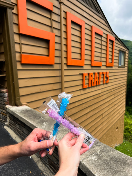 Soco Crafts Maggie Valley NC with two white hands clinking blue and purple rock candy together in front of brown building that says Soco Crafts in orange letters