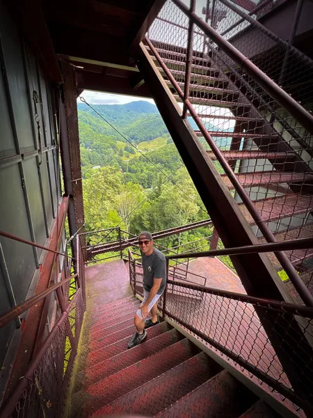 Soco Crafts Tower Maggie Valley Attraction with white brunette male in khaki shorts and tshirt with hat climbing tower stairs