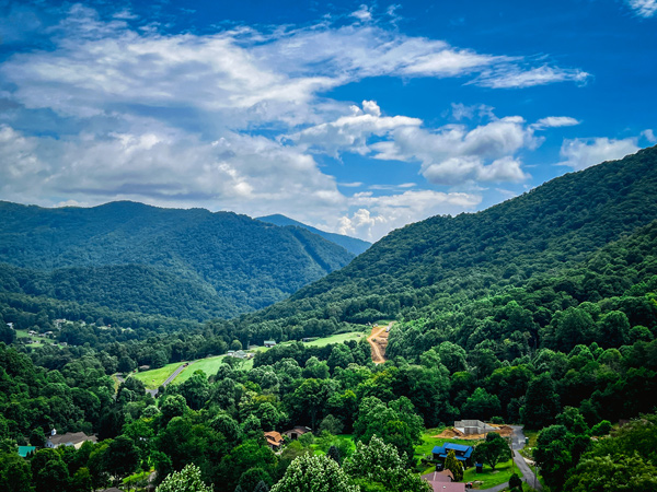 Soco Crafts Tower Maggie Valley NC View with blue and green mountains from 9 story tower on sunny day with clouds in sky and view of Ghost Town in the Sky from a distance