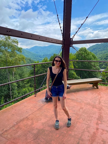 Soco Crafts Tower Maggie Valley North Carolina with white brunette woman in jean shorts and black top with purse and sneakers climbing tower with mountain views