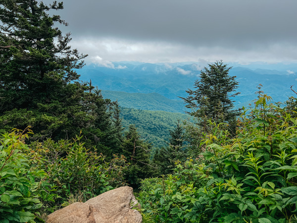 Waterrock Knob Blue Ridge Parkway NC with rock cliff overlooking blue and green mountains with green trees and brush