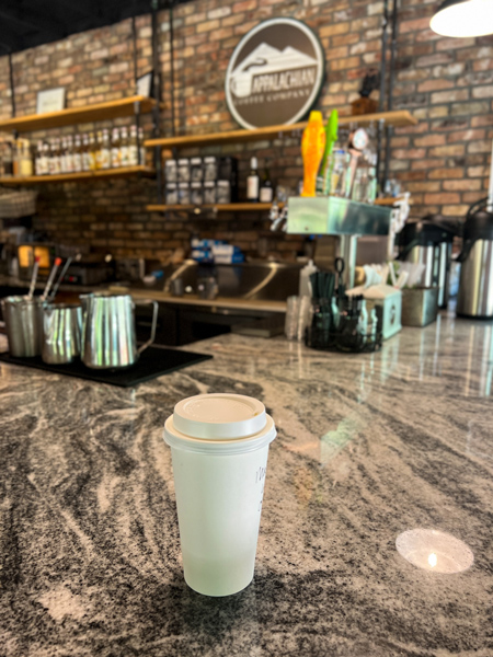 Appalachian Coffee Company Hendersonville Laurel Park NC with white take away coffee cup on counter with taps and coffee machines in the background