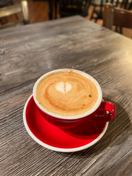 Black Bear Coffee Co Downtown Hendersonville NC with red coffee cup filled with a non-dairy vanilla latte with heart pattern on gray brown table