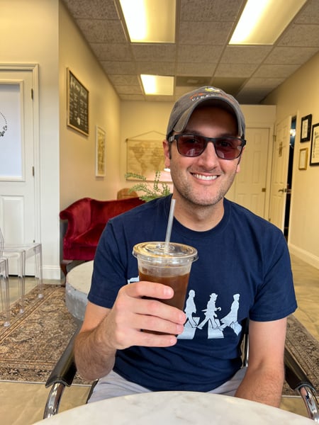 ShareWell Coffee Co Roaster Flat Rock North Carolina with white male in blue shirt, hat, and sunglasses drinking an iced coffee