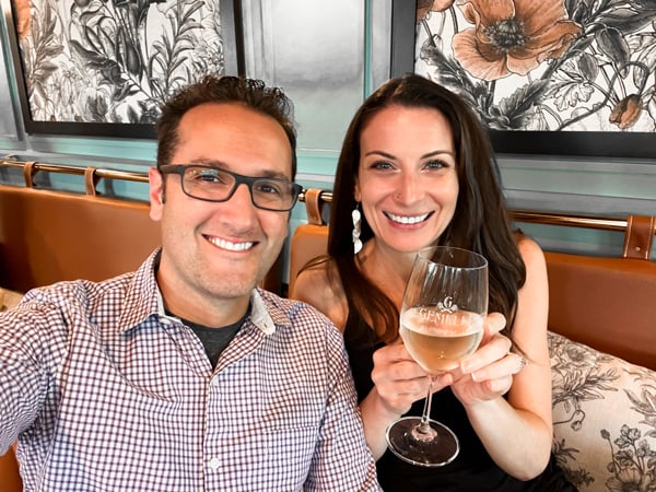 Gemelli Restaurant in Asheville, NC with white brunette male and female dressed up and sitting in nice booth and she is holding a glass of white wine with Gemelli branding on it