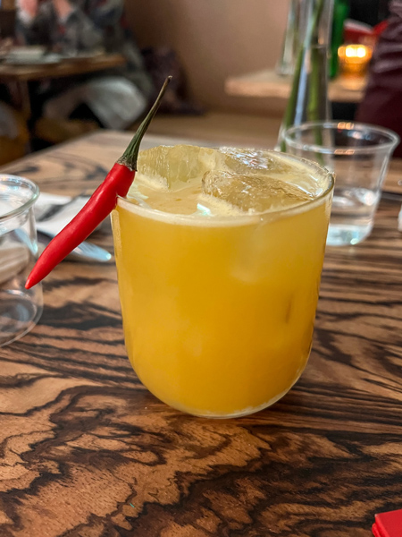 Neng Jrs Restaurant Asheville Cocktail with yellow liquid in low ball glass garnished with a chili pepper on table