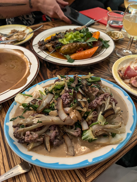 Neng Jrs Restaurant Asheville Veggies on blue and white plate covered in soy like peanut sauce with plate of skewers and more veggies blurred in the background