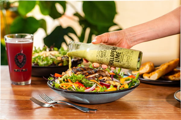 Nine Mile Salad Dressing being poured over salad on brown table with drink in background