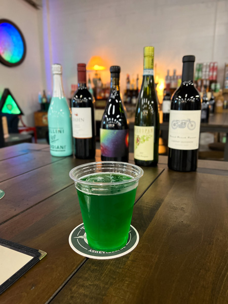 Saint Brighids Bar Marquee Asheville NC with green drink on table in plastic cup with wine bottles in background