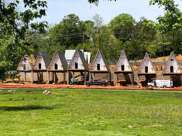 Wrong Way River Lodge & Cabins Asheville NC construction of A-frame housing in front of green grass and above the road