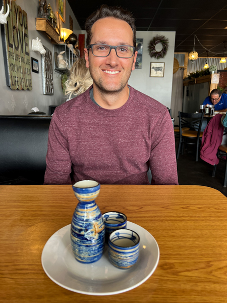 Boon Choo Thai Express Flat Rock NC Hot Sake with two sake glasses in front of white brunette male with glasses in maroon sweater