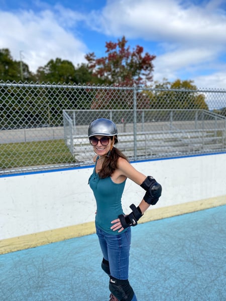 Carrier Park Roller Skating Rink Asheville North Carolina with white brunette female in jeans and green tank top with silver helmet, elbow and knee pads, wrist guards, maroon quad skates, and sunglasses