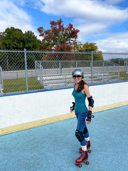 Carrier Park Roller Skating rink in Asheville NC with white brunette female wearing a silver helmet, green tank top, jeans, shoulder and knee pads, wrist guards, and maroon implala quad skates