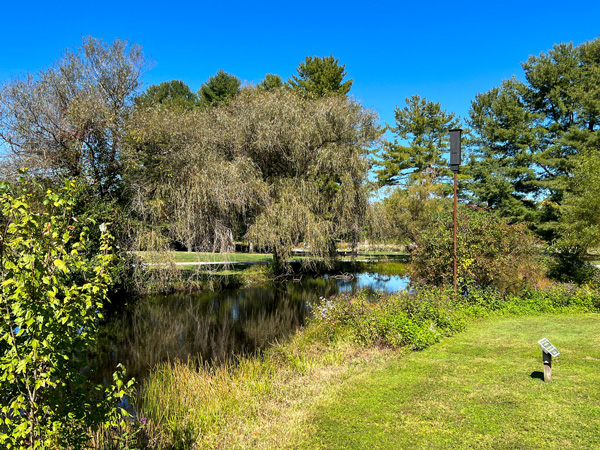 Park at Flat Rock NC Overlook with dark water pond, green grass, and full trees with blue sky