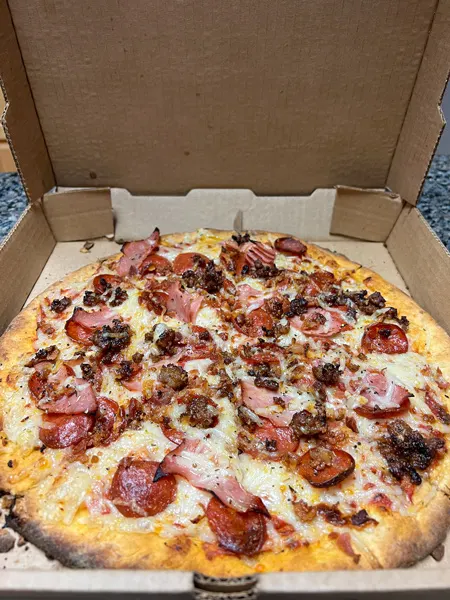 Asheville Pizza and Brewign Gluten Free Pizza with image of large gluten-free pizza crust covered with vegan cheese, sausage, pepperoni, and ham in brown takeout box