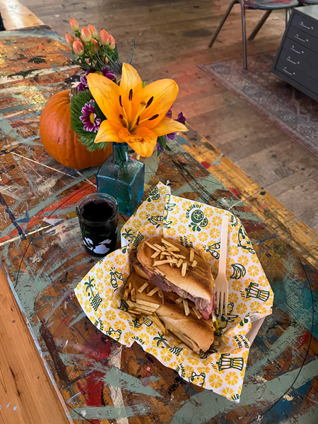 Guajiro Cuban Comfort Food Food Truck Asheville NC with Cuban sandwich topped with small and fried potato shavings on table with yellow flowers