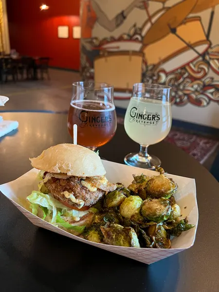 The Smokin Onion Food Truck Gingers Revenge in Asheville with vegan crab cake on bun with fried brussels sprouts on table with mural of woman playing drums in background