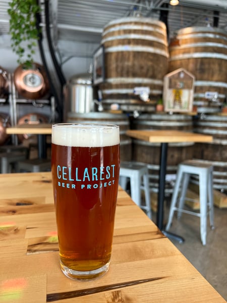 Cellarist Beer Project in Asheville NC with amber gluten-reduced beer on table with barrels and taproom in background