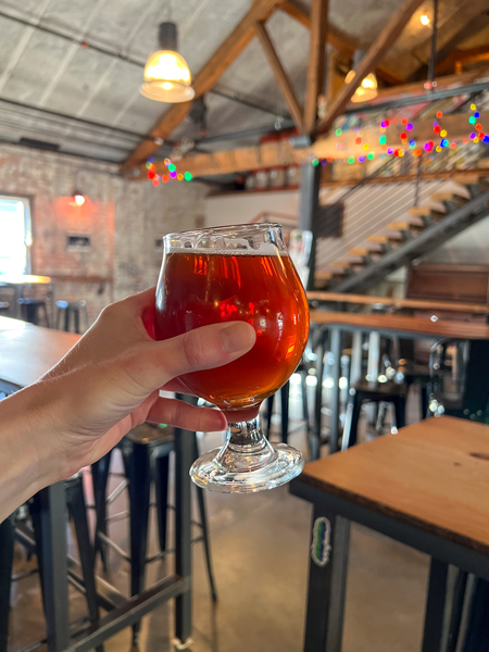 Wedge Brewing in Asheville, NC Foundy Street taproom with white hand holding up amber beer in wood beamed and concrete room