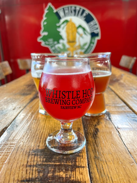 Whistle Hop Brewing Company taproom in Fairview, NC with three red and amber/orange beers on table with logo on red caboose in background