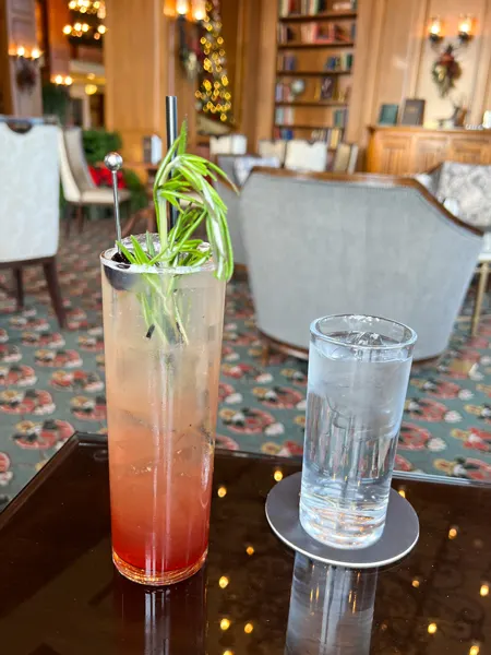 Library Lounge at Biltmore Estate in Asheville NC with glass of water and tall pink cocktail with leafy green garnish on table in library room with books on shelves