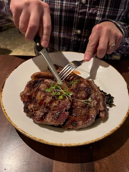 Village Social at Biltmore in Asheville, NC with white male cutting a steak with sweet potatoes on white plate