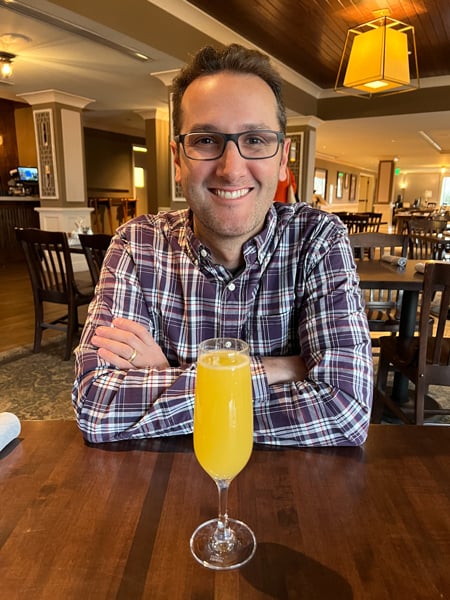 Village Social Biltmore Restaurant Breakfast Mimosa (orange juice and Champange) with Tom, a white brunette male in purple plaid shirt and glasses, sitting at table