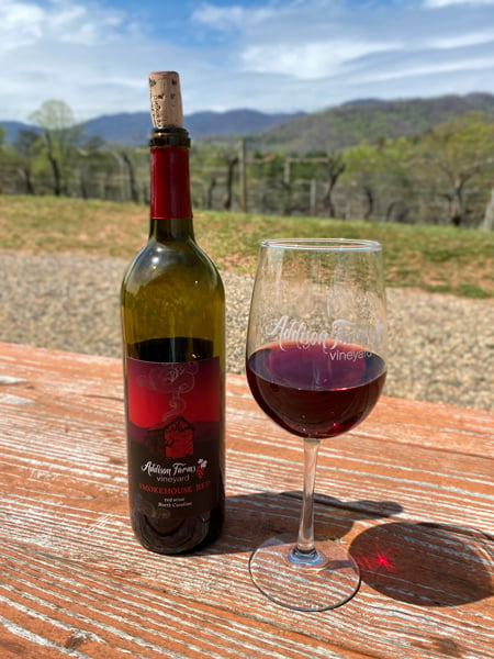 Addison Farms Vineyard in NC red wine bottle next to red glass of wine outside on table overlooking mountains and vineyard