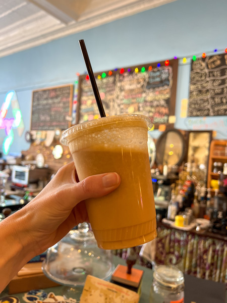 Artisun Gallery and Cafe, Hot Springs, NC banana and peanut butter smoothie in plastic takeaway cup held up in front of blurred menu