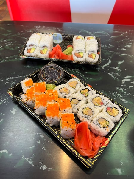 Asaka Japanese Cuisine restaurant in Biltmore Village in Asheville with two takeout containers of sushi on table and containers have salmon, yellow tail, and crab with ginger and wasabi
