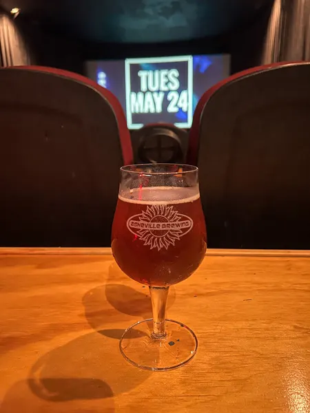 Asheville Pizza & Brewing Movie Theater in Asheville NC with one of their amber beers on table behind movie theater style seats and big screen up front
