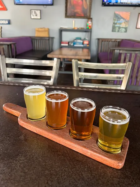 Big Pillow Brewing in Hot Springs, NC flight of beer with yellow, amber, and golden beers in about 5 oz pours sitting on table in taproom with blurred wall art