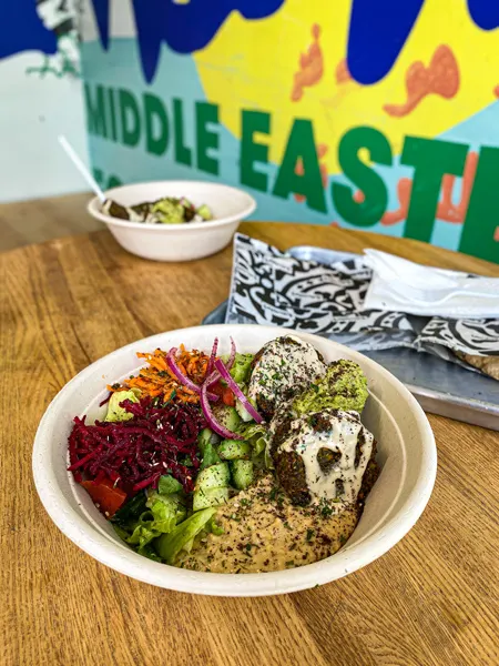 Baba Nahm Middle Eastern Asheville Takeout with bowl on table filled with carrors, red cabbage, falafel, and snowpeas with colorful mural in background