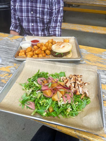 Salad at Haywood Common in Asheville NC with green lettuce, light colored beets, and grilled chicken on plate with second plate of tater tots and gluten-free burger in the background
