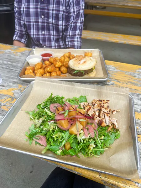 Salad at Haywood Common in Asheville NC with green lettuce, light colored beets, and grilled chicken on plate with second plate of tater tots and gluten-free burger in the background