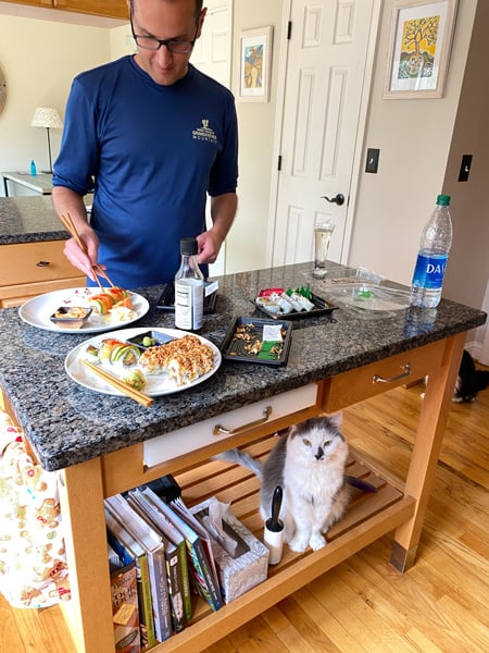 Zen Sushi Takeout in Asheville with white brunette male putting sushi on plates and gray and white cat watching from underneath