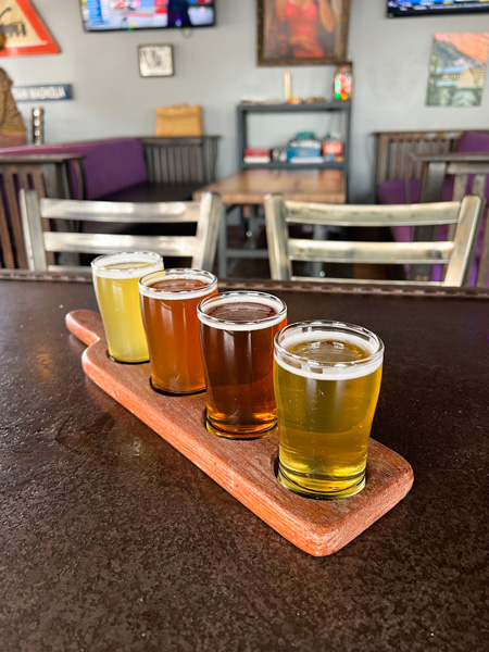 Big Pillow Brewing in Hot Springs, NC Beer Flight with yellow, orange, and brown beers - four of them - on flight board on table in taproom