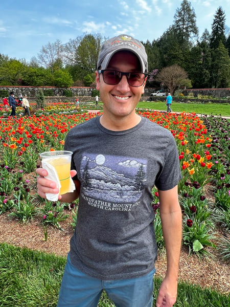Biltmore Blooms Walled Garden with red and yellow tulips and white brunette male with hat, sunglasses, t-shirt and shorts holding a drink in  a plastic cup