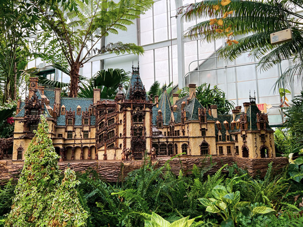 Biltmore Conservatory Model of Biltmore House surrounded by green leaves with greenhouse wall in background
