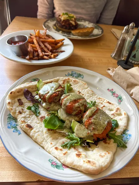 Grateful Organic Diner in Marshall North Carolina Falafel Wrap on plate with three pieces of brown falafel with green lettuce on a pita like bread and fries in separate bowl in background
