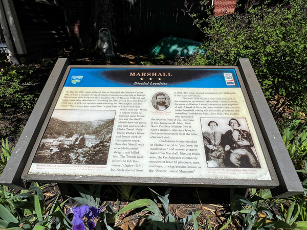 Historic Downtown Marshall, NC Educational sign along sidewalk and surrounded by flowering bush talking about the history of Marshall during the Civil War