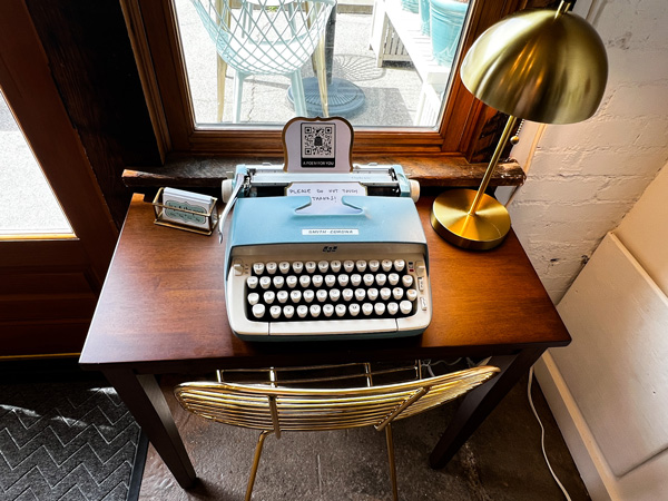 Ivy and the Poet in Marshall NC with blue old school typewriter on brown desk with brass lamp