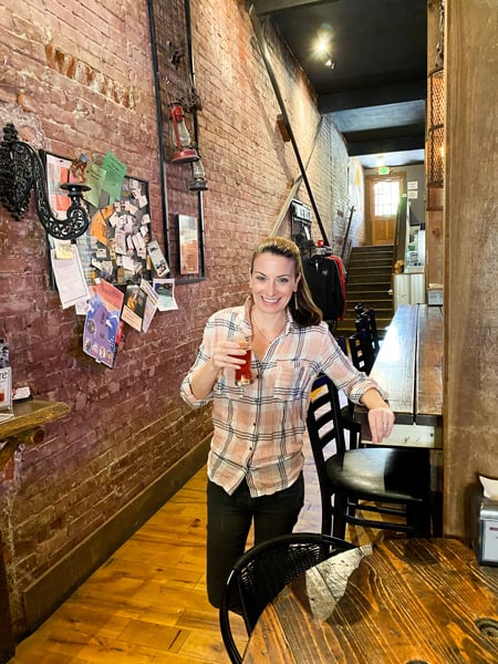 Mad Co. Brew House in Downtown Marshall taproom with white brunette woman in pink and gray plaid shirt with gray jeans holding a strawberry beer