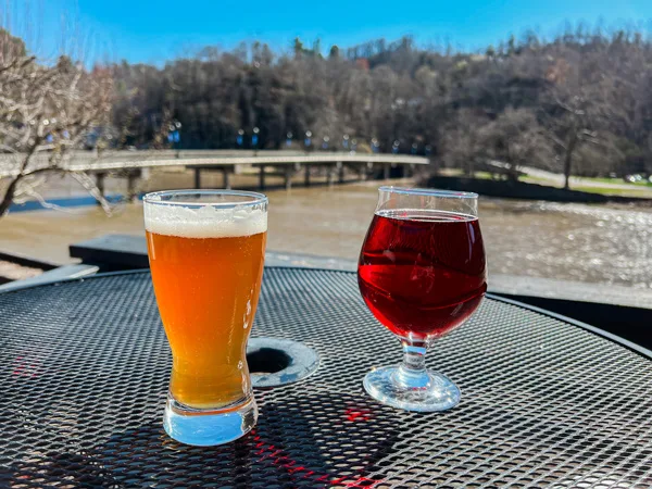 Mad Co. Brew House in Marshall North Carolina with yellow orange beer and red cider on table outdoors overlooking bridge and French Broad River