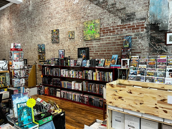 Main Street Comics and Games in Marshall North Carolina with white and redish brick wall and low bookshelf filled with graphic novels