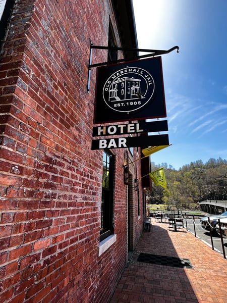 Old Marshall Jail Hotel in Marshall NC with facade of historic brick building with sign that says hotel and bar and French Broad River in the background